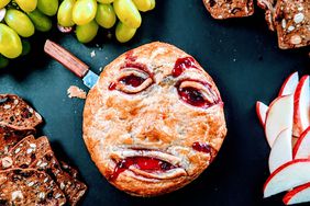 Halloween baked Brie decorated to resemble a bloody face on snack board with fruit and crackers