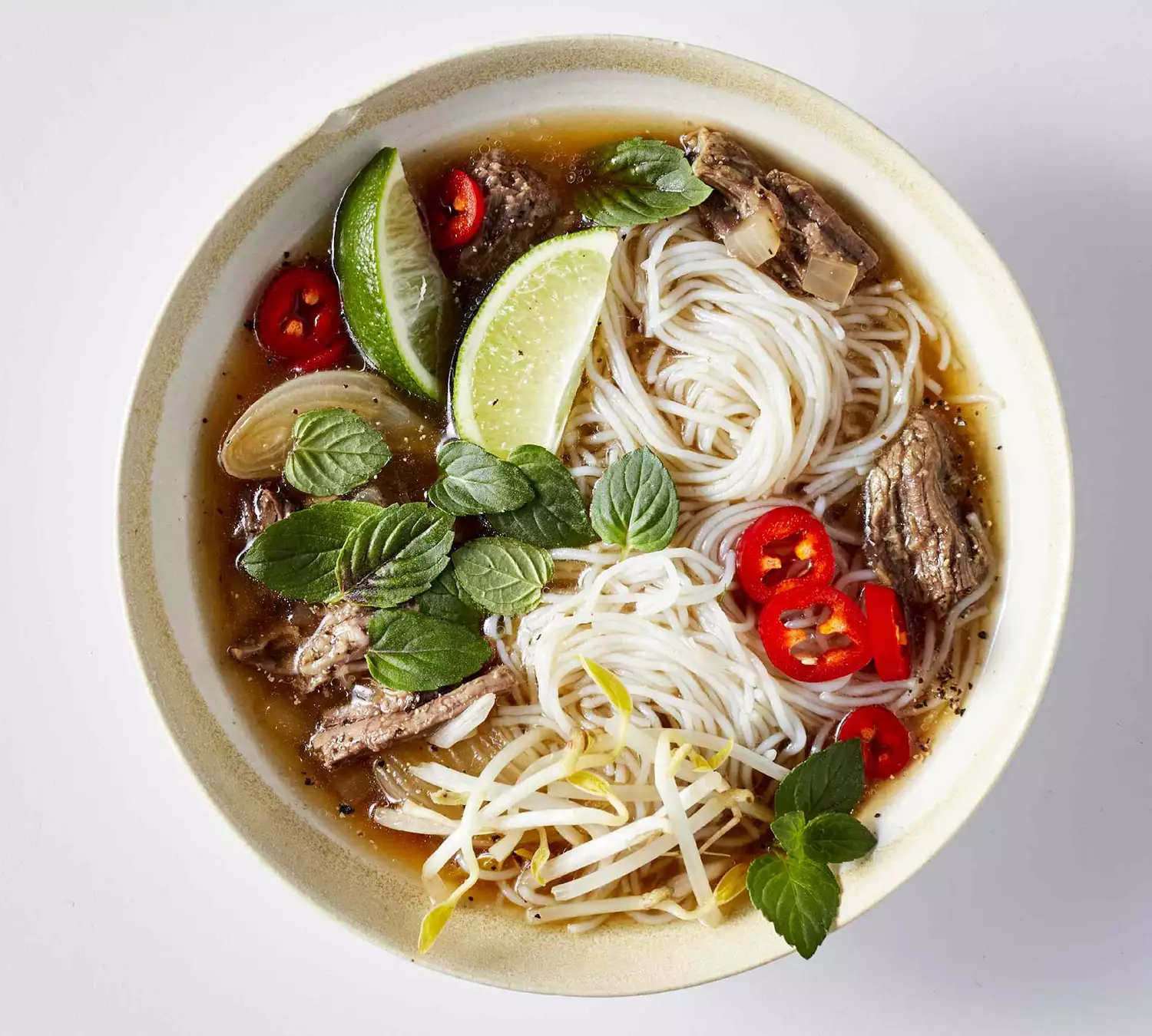 pho with beef, rice noodles, lime, and peppers in clay bowl