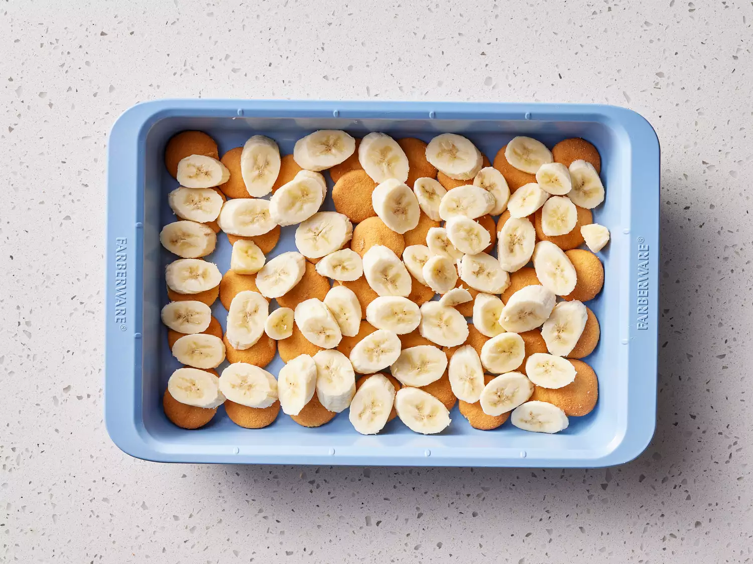 A rectangle baking dish with round, vanilla cookies topped with sliced bananas