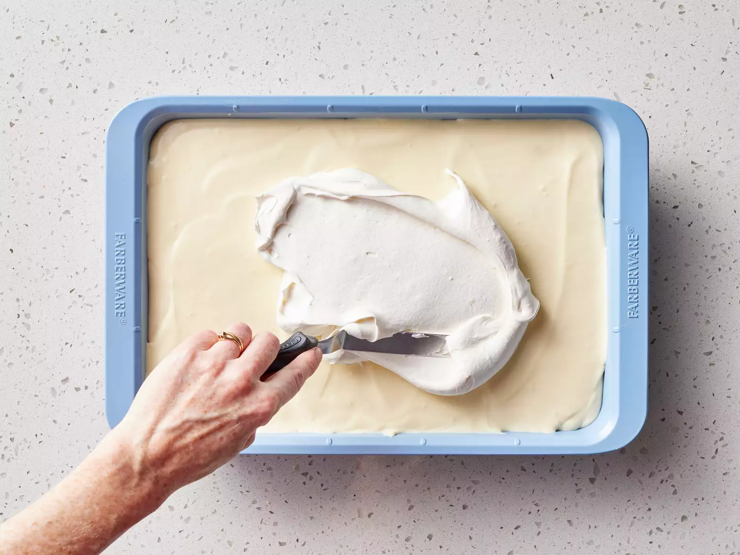 An offset spatula spreading whipped topping over a pan of banana pudding