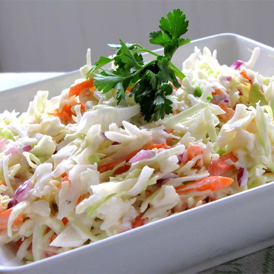 A white bowl filled with creamy coleslaw made with shredded carrots and green cabbage