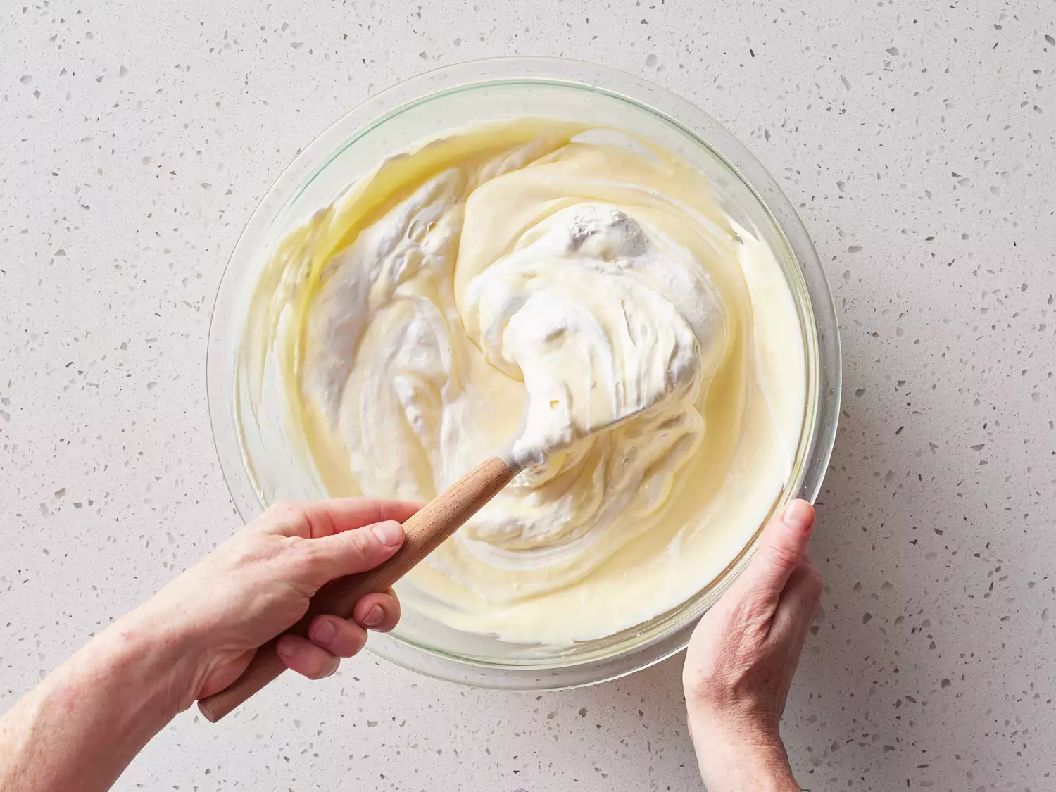 A spatula folding in whipped topping into a bowl of vanilla pudding
