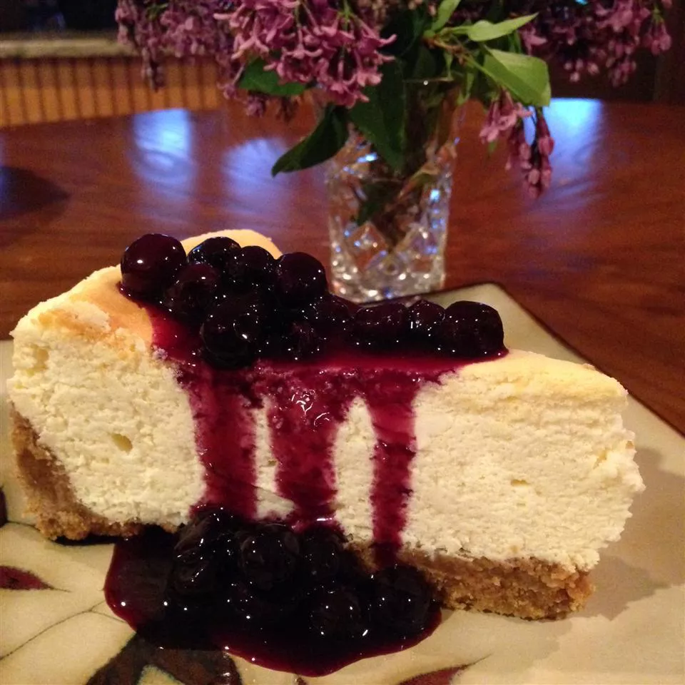 slice of lemon cheesecake with blueberries on top and vase of flowers in background