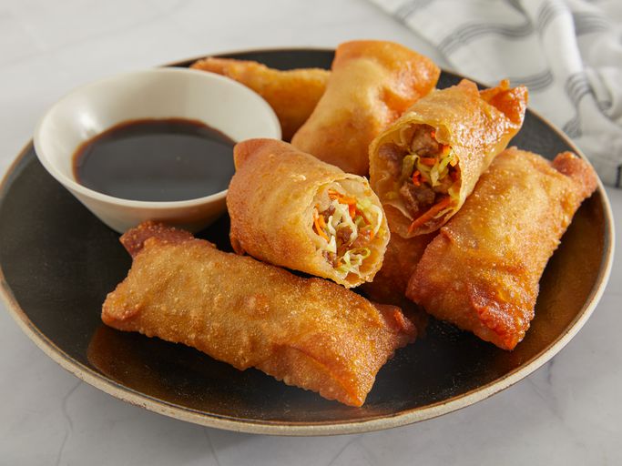 looking into a plate of egg rolls with one cut open, served with a side of soy sauce
