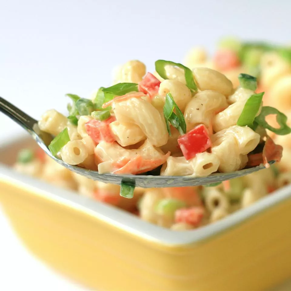 closeup of a spoonful of macaroni salad being scooped from a square yellow bowl